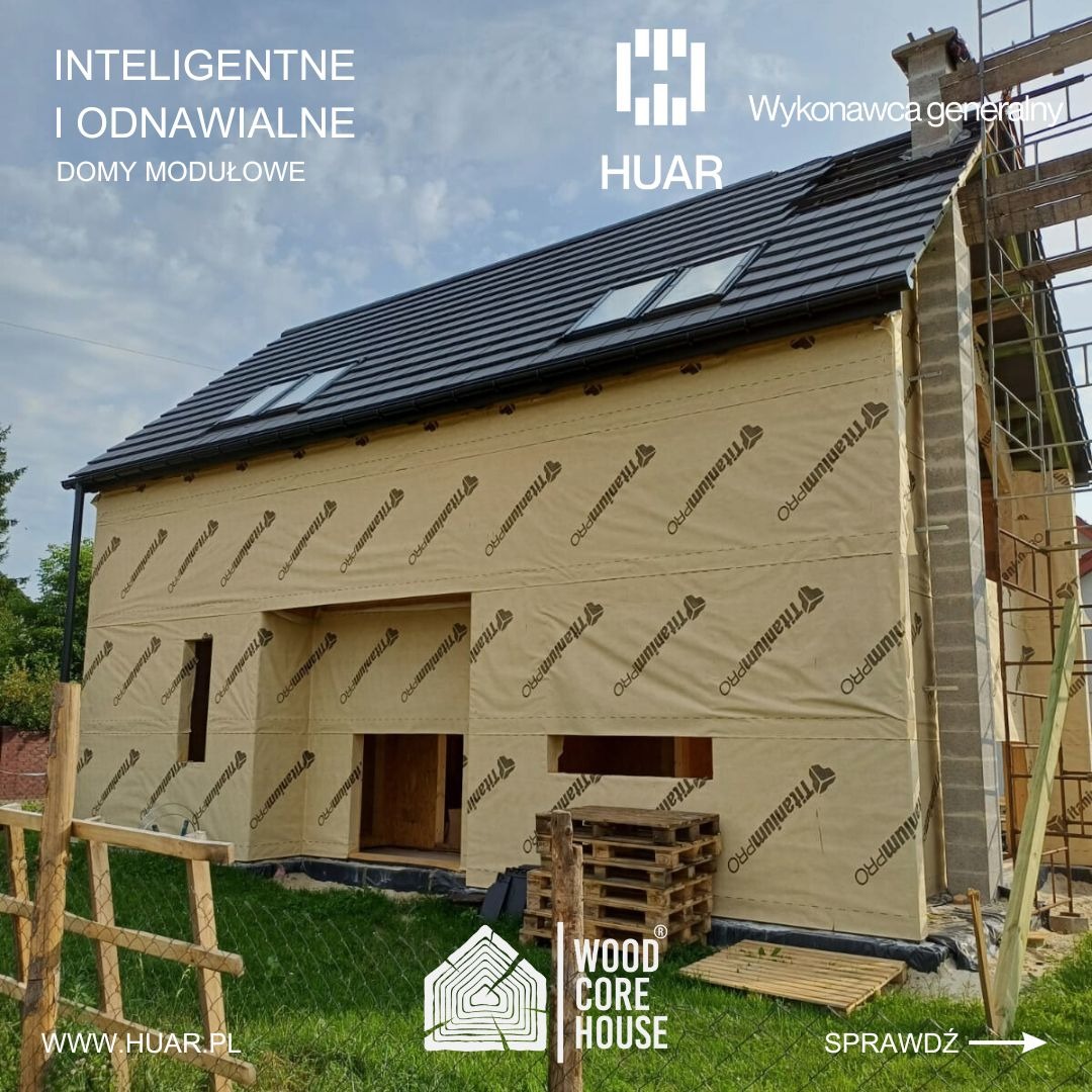 Wznoszony dom modułowy z widoczną konstrukcją pokrytą membraną TitaniumPRO, na tle częściowo zachmurzonego nieba, z widocznymi paletami drewnianymi i fragmentem ogrodzenia.