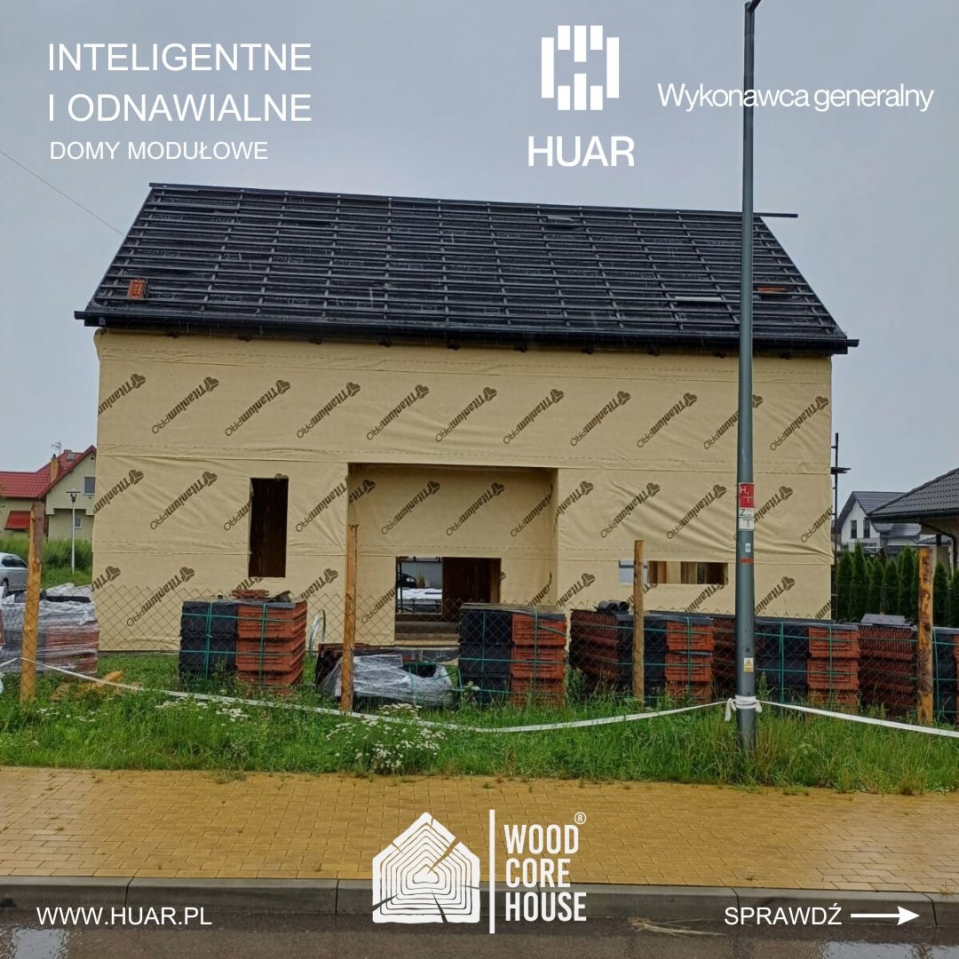 Budowa domu w trakcie realizacji, z widoczną izolacją ścian zewnętrznych marki TitaniumPRO, częściowo pokrytym dachem i stertami dachówek przed budynkiem, sfotografowany w pochmurny dzień.