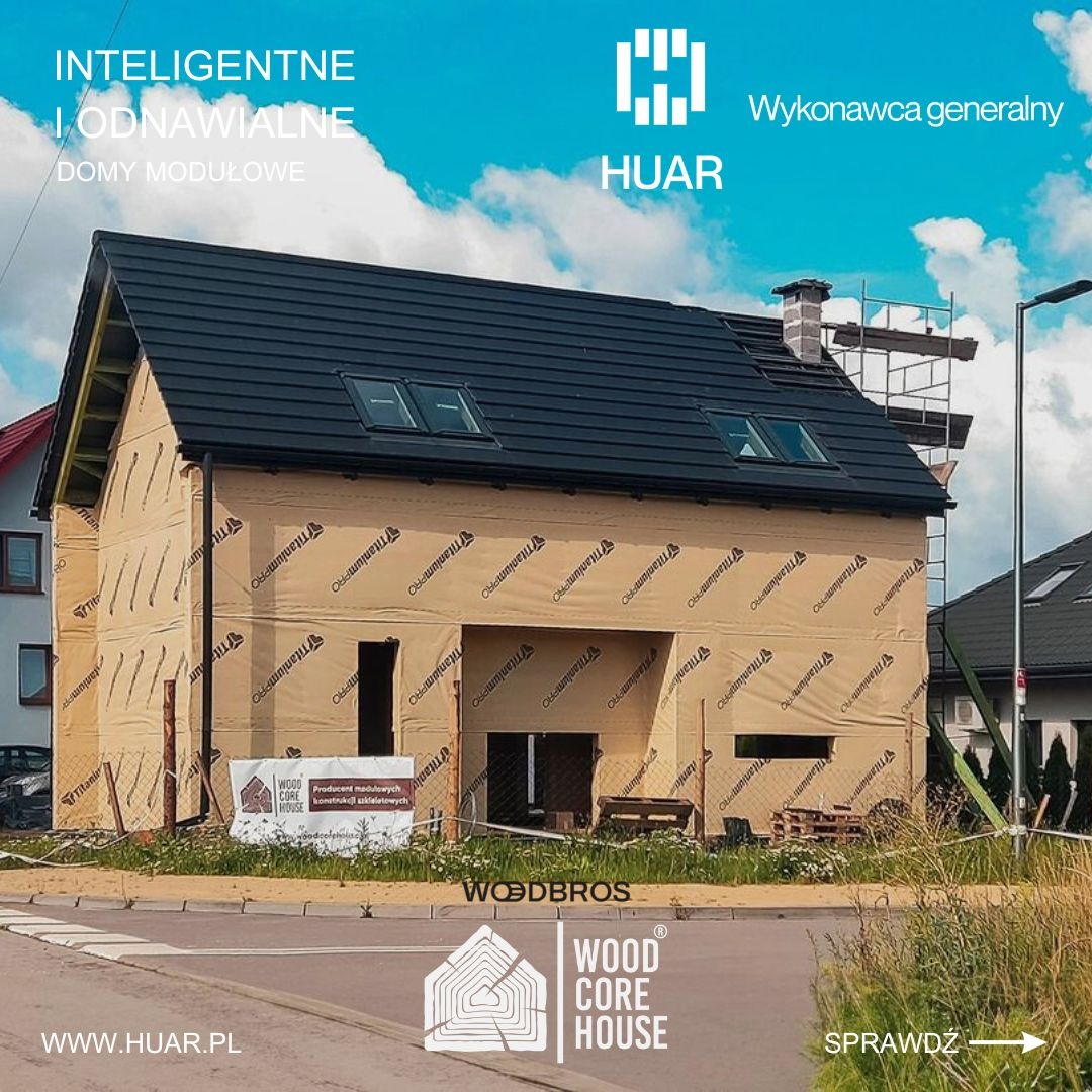 Niedokończony dom z czarnym dachem i oknami dachowymi, pokryty membraną wiatroizolacyjną, widoczny na tle błękitnego nieba z logotypami firm budowlanych na pierwszym planie.