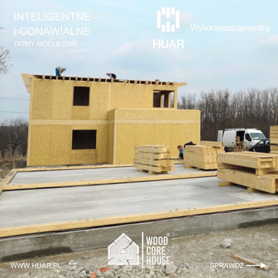 Wznoszenie dwukondygnacyjnego domu z drewnianych paneli na betonowej płycie fundamentowej, widoczni dwaj pracownicy na dachu, przygotowane drewniane elementy konstrukcyjne obok, firmowy van w tle.