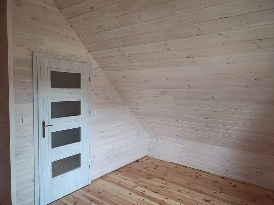 Wnętrze poddasza wykończonego boazerią w jasnym odcieniu, z drewnianą podłogą i drzwiami wewnętrznymi z czterema szybami.