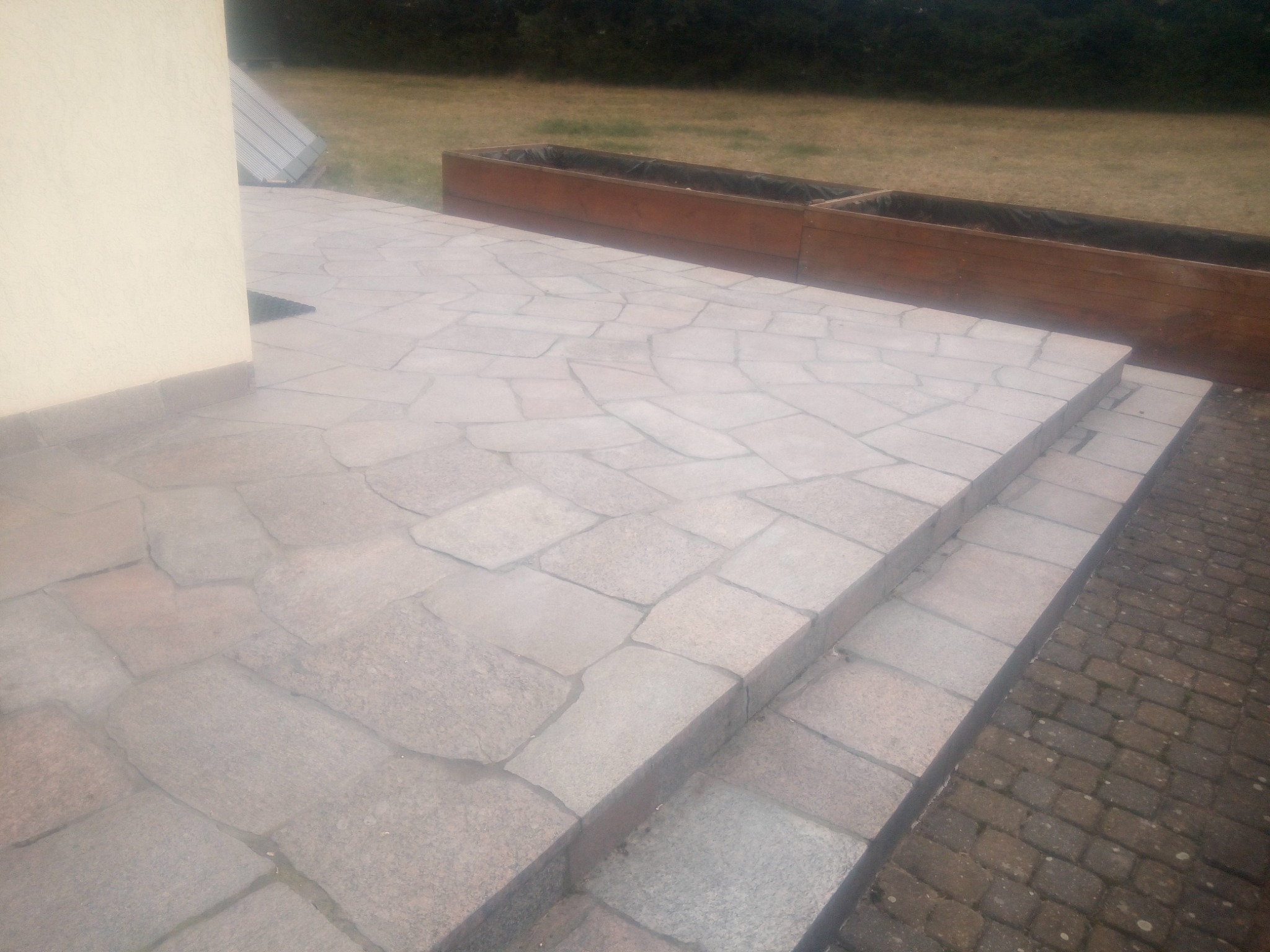 Kamienny taras z dwoma stopniami w Goniądzu, prowadzący do drewnianej skrzyni na rośliny, widok z boku.