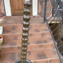 Elastyczny wał do udrażniania rur, pokryty ciemnym osadem, umieszczony na zewnątrz, na tle schodów z płytek i kutych balustrad.