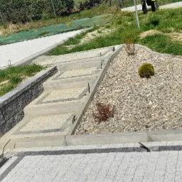 Schody z kostki brukowej prowadzące przez skalniak z drobnymi krzewami i wysypanym grysem, w tle widoczny fragment ścieżki z kostki brukowej i trawnik.