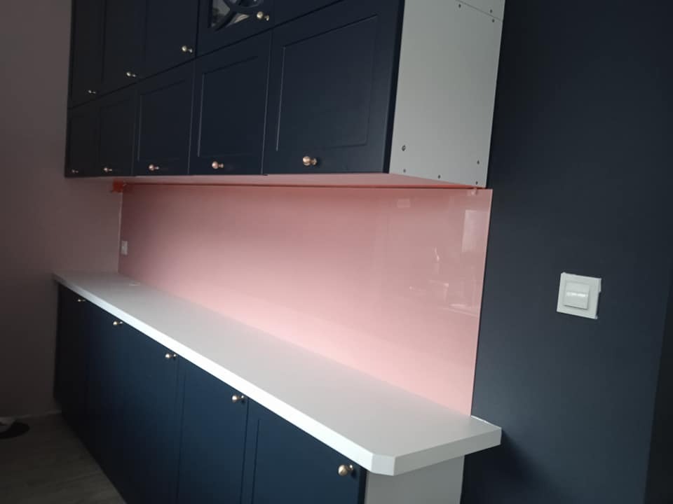 Kuchnia z granatowymi szafkami i bladoróżowym panelem szklanym między blatem a szafkami wiszącymi.
