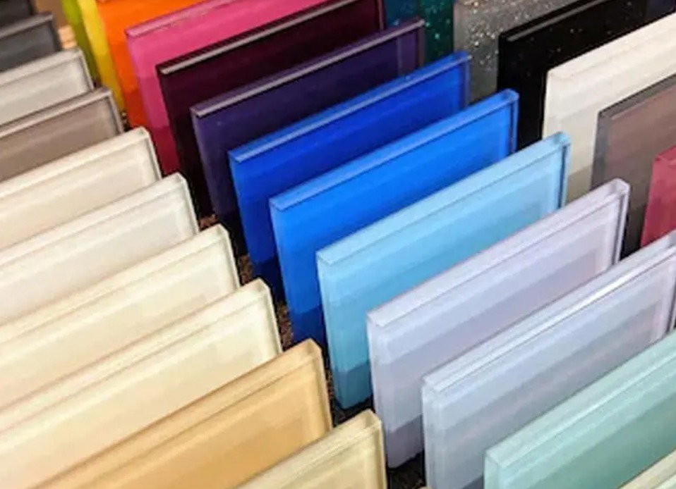 Paleta kolorowych szklanych paneli w odcieniach beżu, błękitu, fioletu, pomarańczy i czerni ułożonych rzędami, prezentująca różnorodność barw i wykończeń szkła.