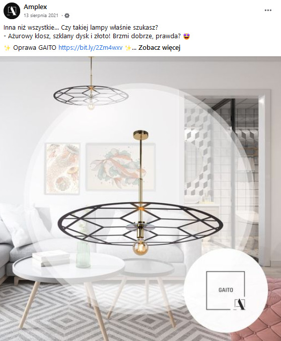 Nowoczesna lampa wisząca z ażurowym, geometrycznym kloszem w kolorze czarnym i złotym, zawieszona nad białym stolikiem w jasnym wnętrzu z elementami dekoracyjnymi.