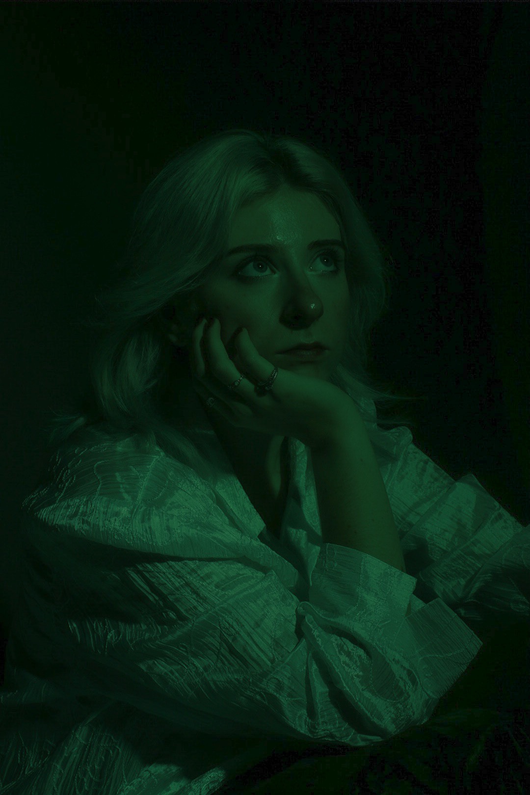 Portret kobiety z blond włosami, opierającej brodę na dłoni, zamyślona, oświetlona zielonym światłem