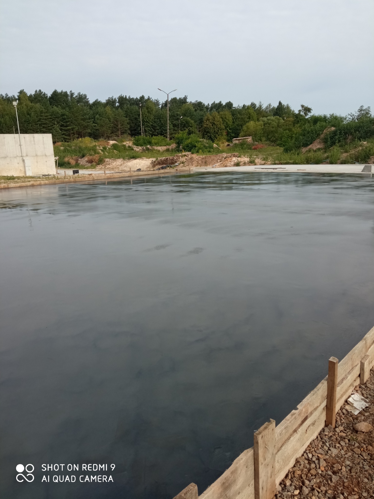 Świeżo wylana, gładka powierzchnia posadzki w Lublinie, otoczona drewnianym szalunkiem, z widocznym tłem zieleni drzew.