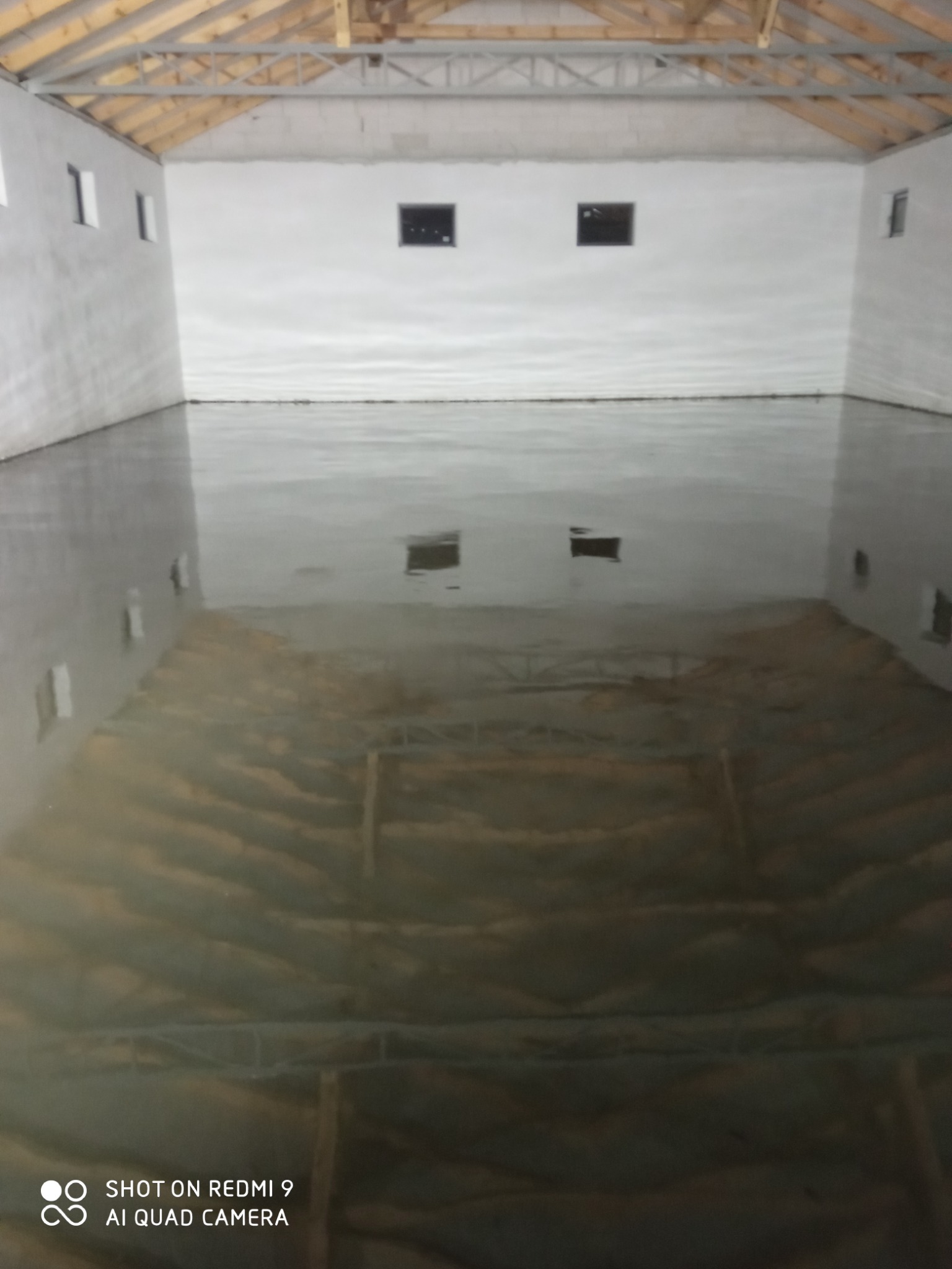 Wnętrze hali z wylewką jastrychową w trakcie schnięcia, widoczne drewniane elementy konstrukcji dachu i małe okna w ścianach.