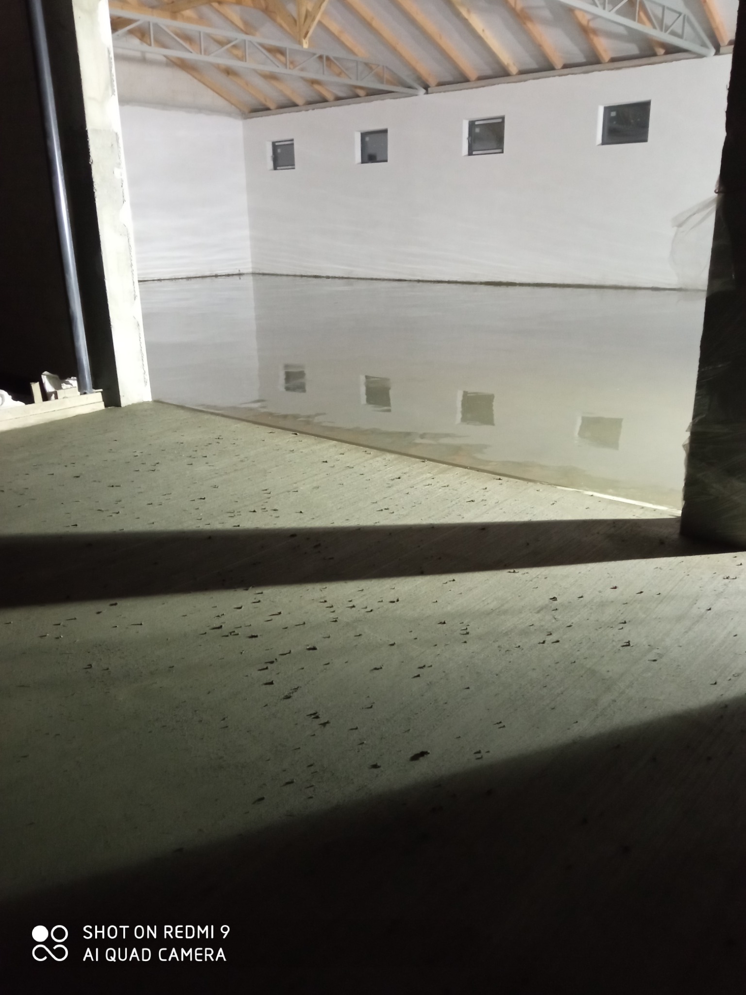 Świeżo wylana, gładka posadzka w hali przemysłowej, widoczne okna w ścianie i konstrukcja dachu