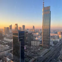 Panorama Warszawy o wschodzie słońca, widok z wysokości na drapacze chmur, ulice i parkingi.