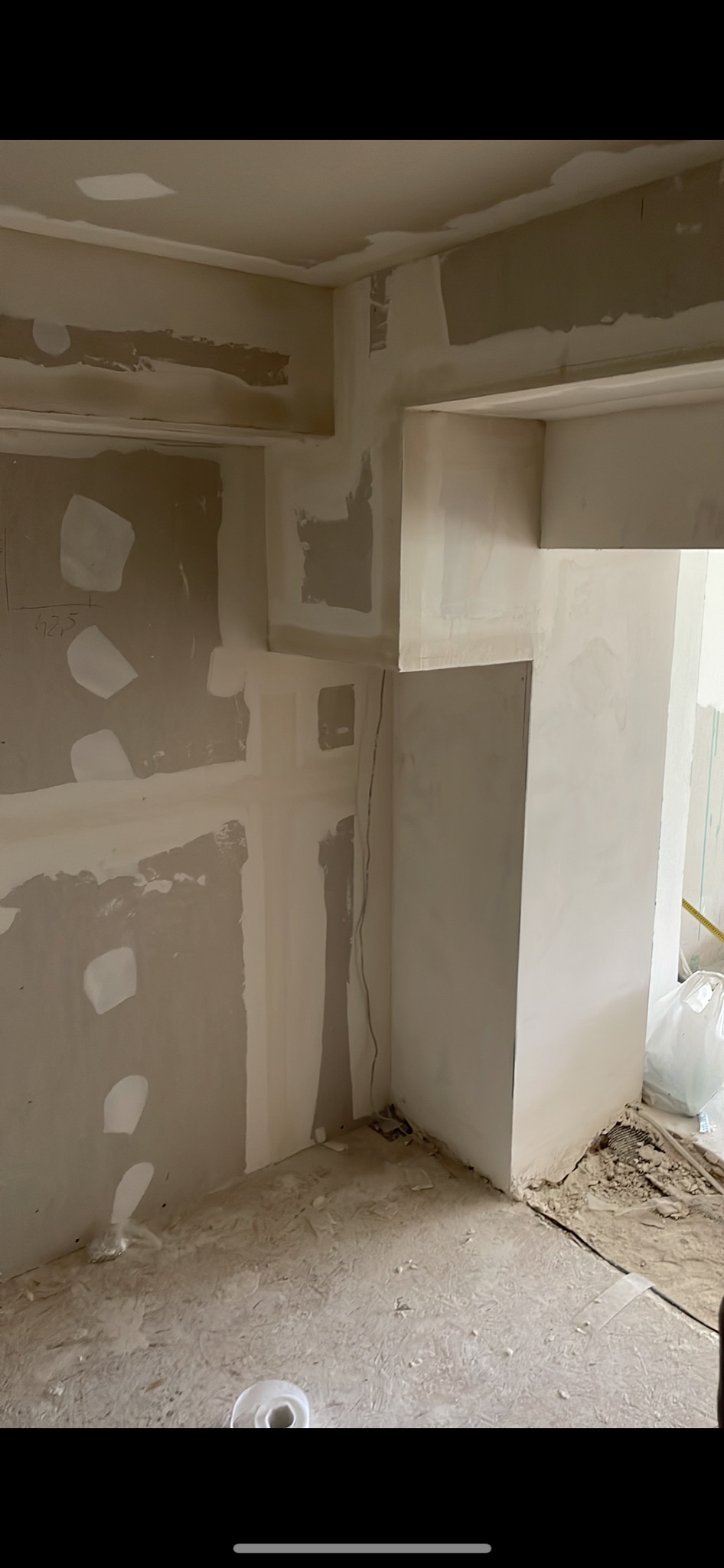 Wnętrze w trakcie prac wykończeniowych, ściany pokryte gładzią szpachlową, widoczne fragmenty płyty OSB na podłodze oraz wystające kable elektryczne.