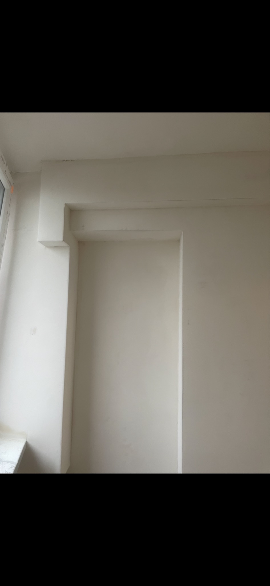 Wnęka w ścianie wykończona płytą karton-gips, pomalowana na biało, widoczna z bliska, z fragmentem okna po lewej stronie.