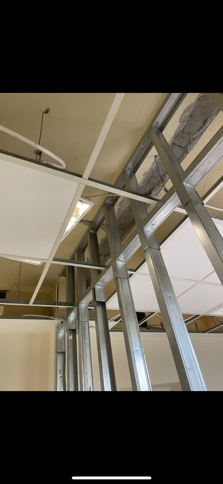 Metalowa konstrukcja sufitu podwieszanego z widocznymi elementami instalacji i fragmentami uszkodzonego stropu.