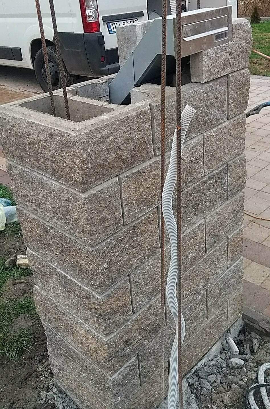 Murowany słupek z pustaków z widoczną skrzynką na listy w trakcie budowy w Kielcach, wystające pręty zbrojeniowe i peszel elektryczny.