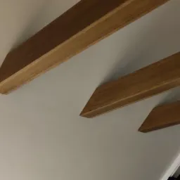 Nowoczesna antresola z drewnianymi belkami stropowymi, widok od dołu na białą ścianę i okno.