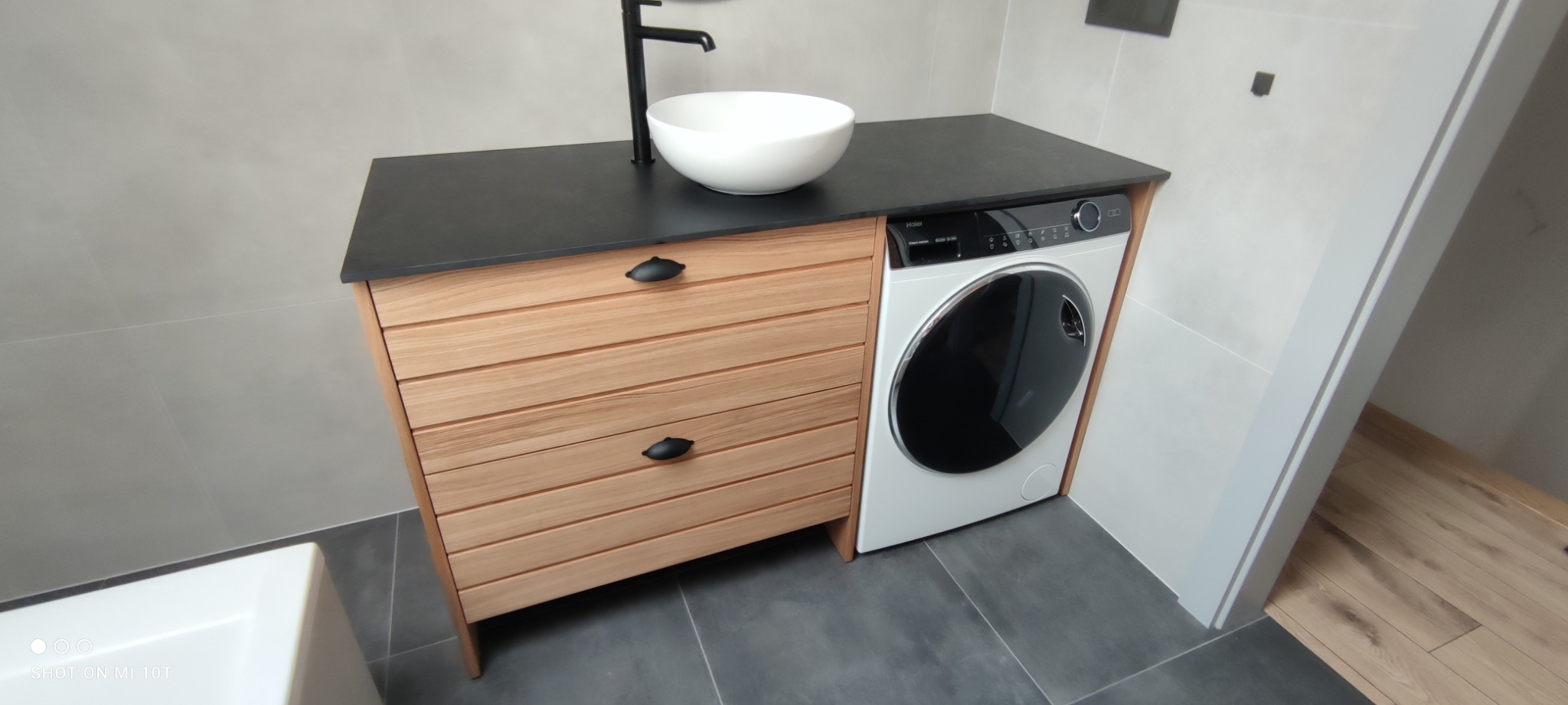 Łazienka w Barwałdzie Średnim z drewnianą szafką z szufladami pod umywalką nablatową i pralką automatyczną w zabudowie, czarny blat.