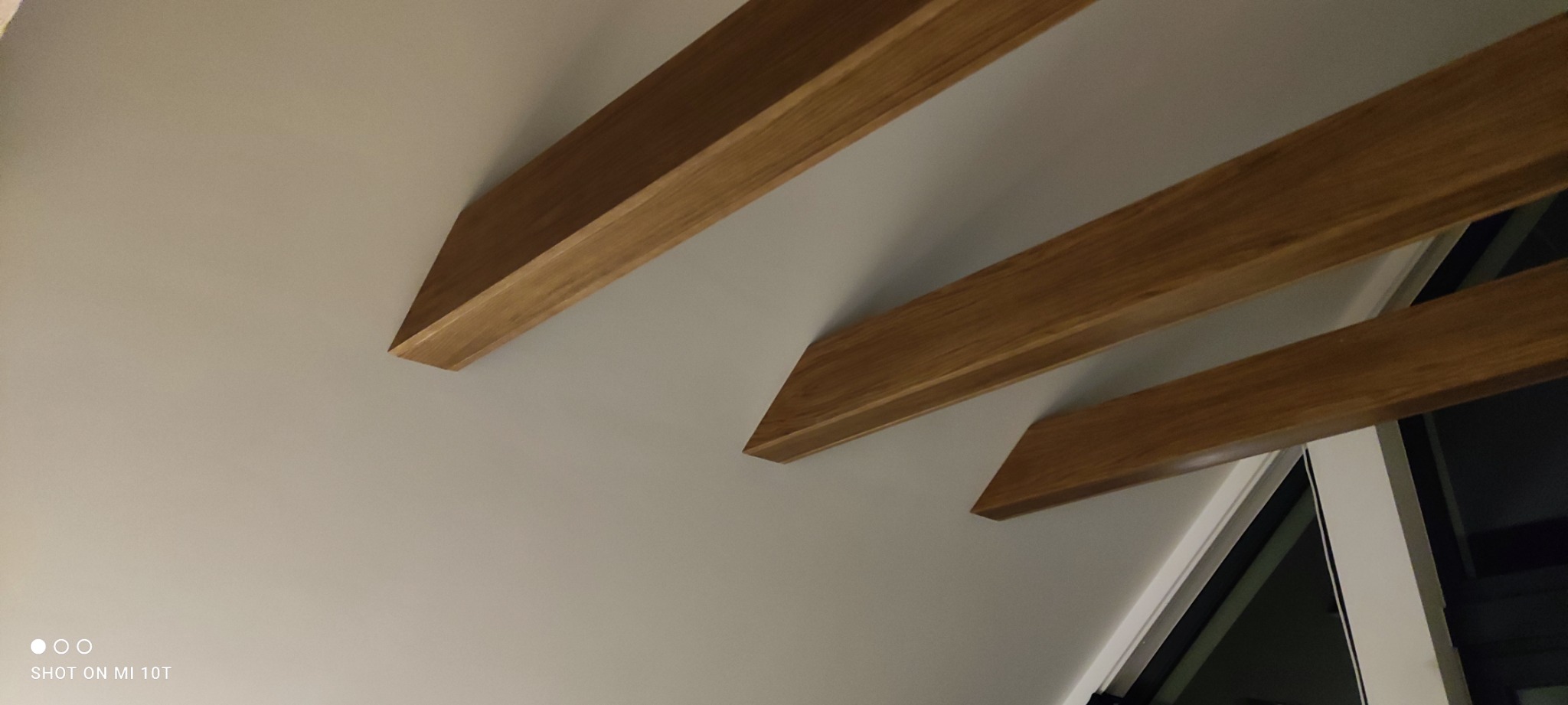 Nowoczesna antresola z drewnianymi belkami stropowymi, widok od dołu na białą ścianę i okno.