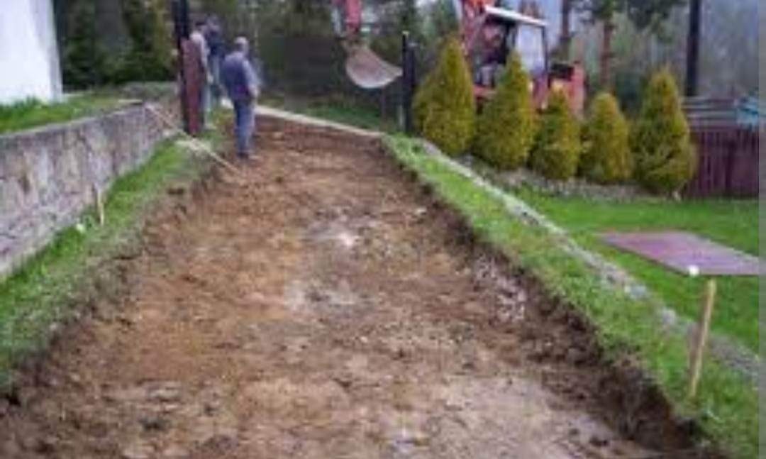 Przygotowanie terenu pod budowę drogi: wykopana ziemia, widoczny fragment koparki i grupa osób nadzorujących prace.