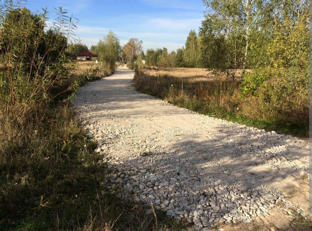Ścieżka gruntowa wysypana gruzem i kamieniami w wiejskim krajobrazie, widok perspektywiczny w słoneczny dzień.