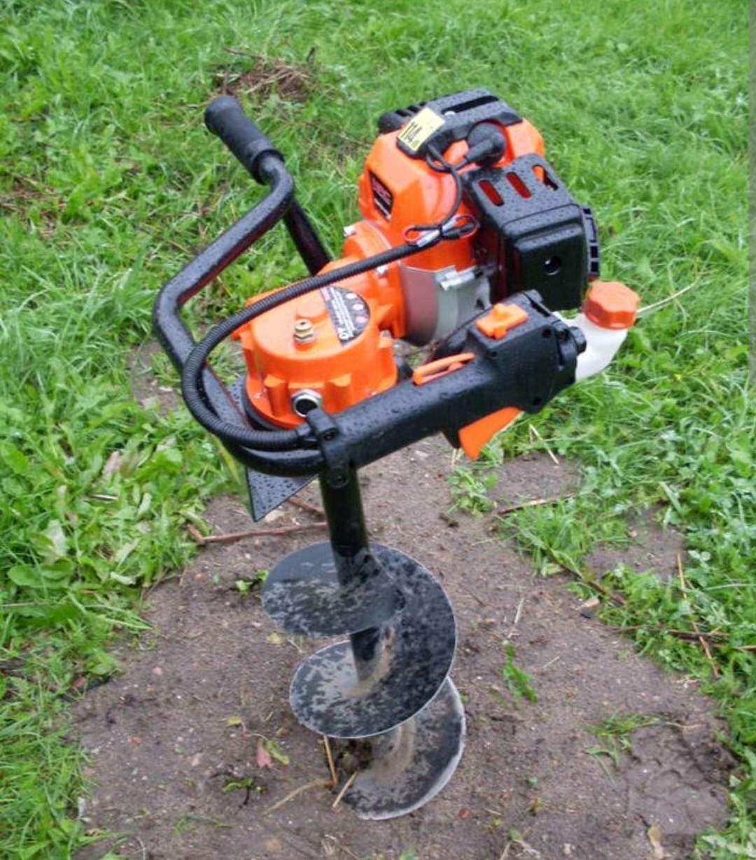 Pomarańczowo-czarny świder glebowy spalinowy z mokrą od ziemi spiralą w Wadowicach, stojący na trawie.