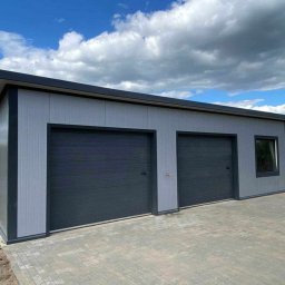 Nikmet Marcin Nikodem - Nowoczesny garaż blaszany z dwoma bramami segmentowymi w kolorze grafitowym, wykończony panelami w odcieniach szarości, na tle błękitnego nieba z chmurami.