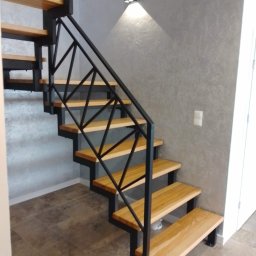 Nikmet Marcin Nikodem - Nowoczesne schody metalowe z drewnianymi stopniami i geometryczną balustradą w jasnym wnętrzu. Minimalistyczny design, oświetlenie punktowe.