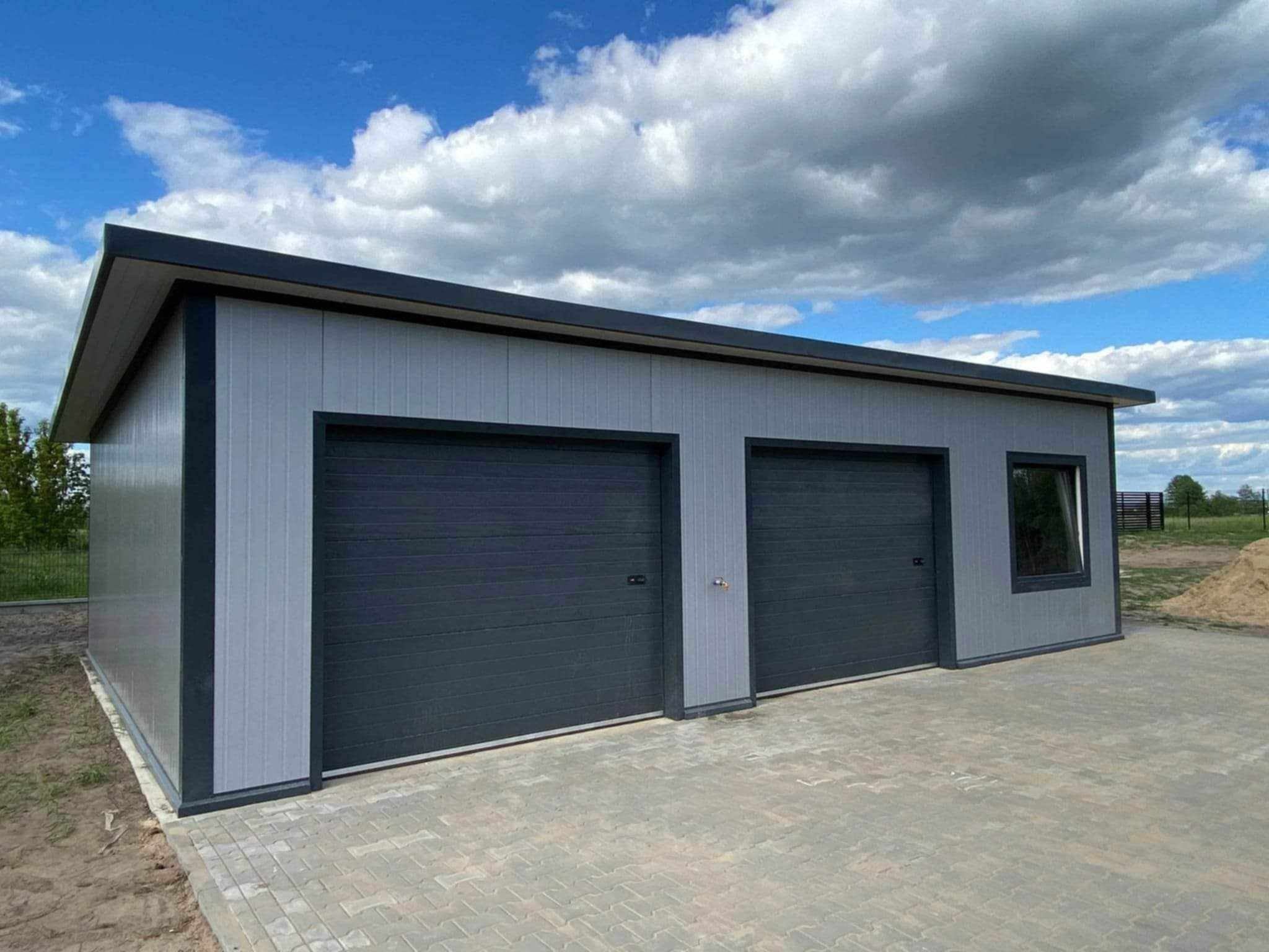 Nowoczesny garaż blaszany z dwoma bramami segmentowymi w kolorze grafitowym, wykończony panelami w odcieniach szarości, na tle błękitnego nieba z chmurami.