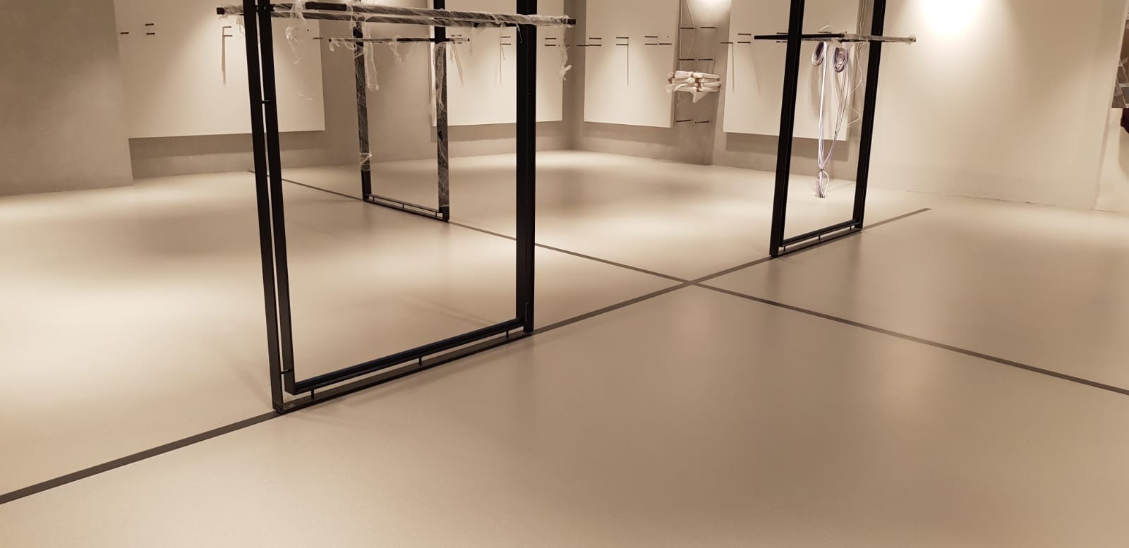 Jasna, gładka posadzka z zaznaczonymi czarnymi liniami podziału, w tle białe ściany i metalowe stelaże na ubrania w nowym sklepie.