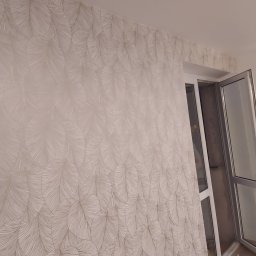 Tomasz Matlak - Ściana pokryta tapetą w delikatny, piórkowy wzór, z fragmentem niezakończonego montażu na górze, przylegająca do otwartego okna balkonowego z białymi ramami.