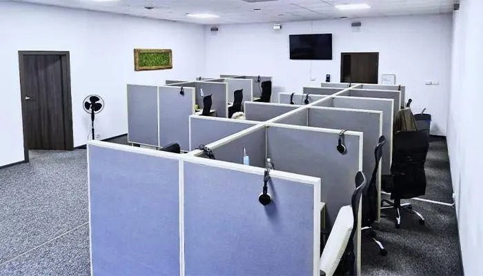 Przestrzeń biurowa z boksami dla pracowników, wyposażona w słuchawki, z dekoracją w postaci zielonego panelu na ścianie i telewizora.