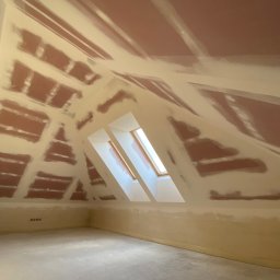 REMPROF - Poddasze z oknami dachowymi w trakcie prac wykończeniowych; widoczne fragmenty płyt gipsowo-kartonowych pokryte warstwą szpachli, przygotowane do dalszej obróbki.