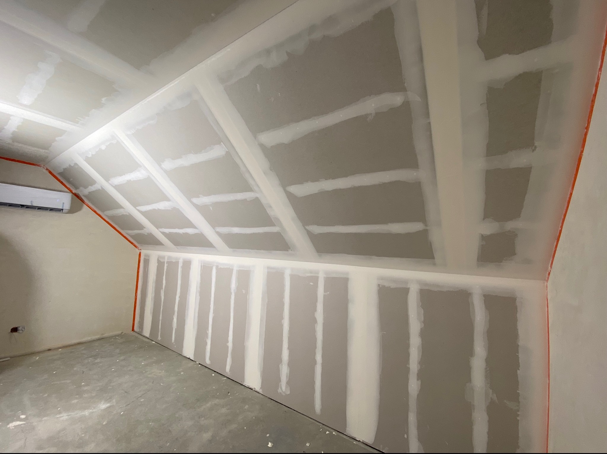 Poddasze z ukośnym sufitem w trakcie montażu płyt kartonowo-gipsowych, widoczne łączenia wypełnione masą szpachlową, pomarańczowe zabezpieczenia narożników.