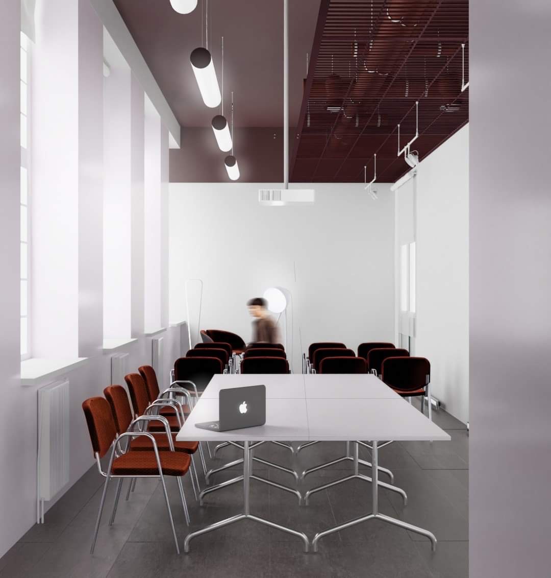 Minimalistyczna sala konferencyjna z białym stołem, pomarańczowymi krzesłami i laptopem, oświetlona podłużnymi lampami i z kratownicowym sufitem w odcieniach brązu.