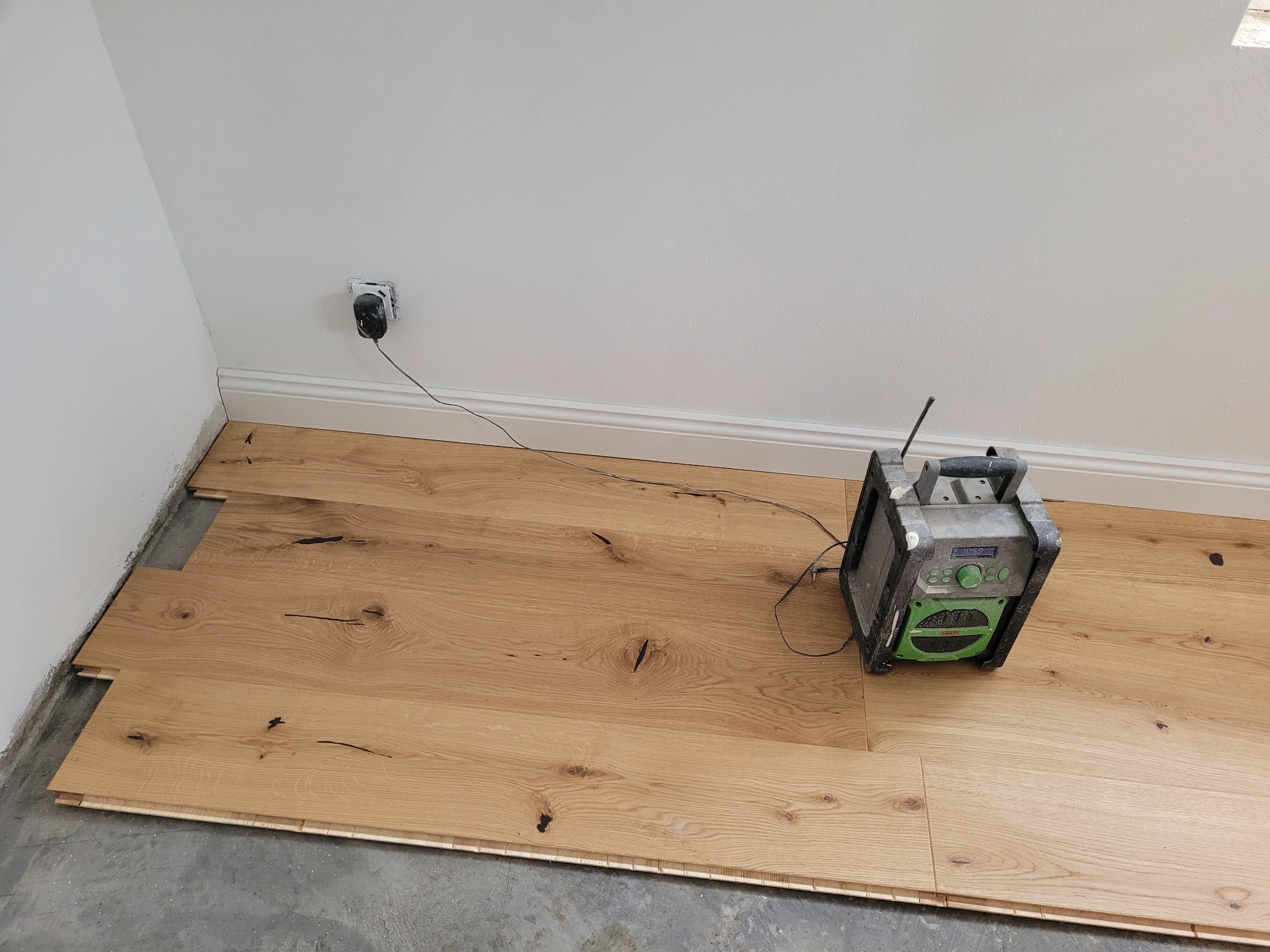 Fragment układania jasnego parkietu z widocznym radiem budowlanym i niedokończonymi krawędziami przy ścianie.