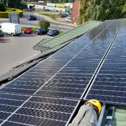 Montaż paneli słonecznych na zielonym dachu; w tle widoczny parking, rondo i zabudowa miejska.