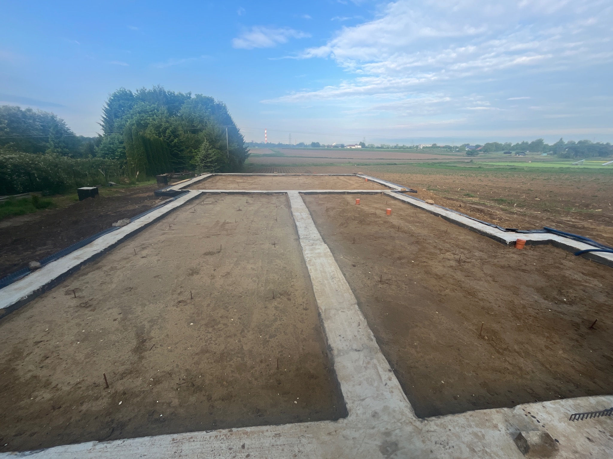 Fundamenty domu jednorodzinnego w Myślenicach, widziane z góry. Betonowe ławy fundamentowe, przygotowane do dalszych prac budowlanych, otoczone ziemią.