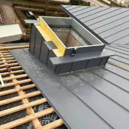 Montaż blachy trapezowej na dachu z oknem dachowym i izolacją, widoczne narzędzia i elementy konstrukcyjne