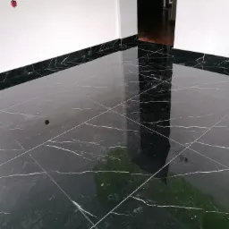 Błyszcząca, czarna marmurowa podłoga z białymi żyłkami, widok na białe ściany i otwarte drzwi do ciemnego pomieszczenia, kabel elektryczny wystający ze ściany.