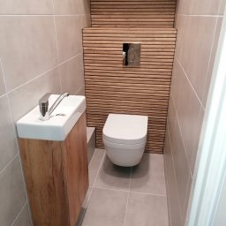 Usługi wykończeniowo-hydrauliczne - Nowoczesna toaleta z umywalką na drewnianej szafce i dekoracyjną ścianą z poziomych listew drewnianych.