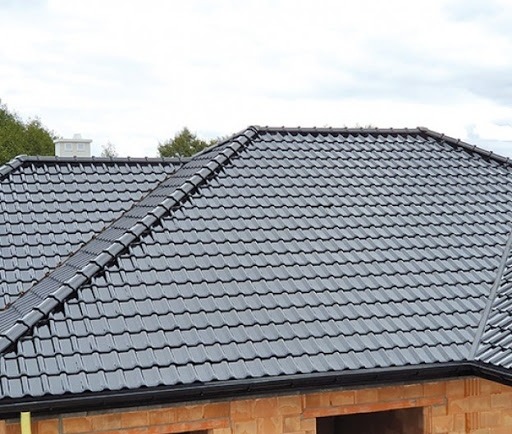 Nowy, grafitowy dach z dachówki ceramicznej na surowej konstrukcji budynku z cegły, widok z góry w pochmurny dzień.