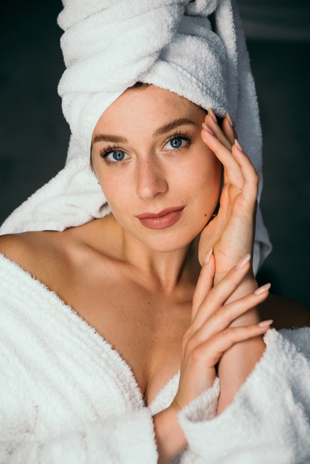 Portret kobiety w białym szlafroku i ręczniku na głowie, z delikatnym makijażem i naturalnym światłem podkreślającym rysy twarzy.