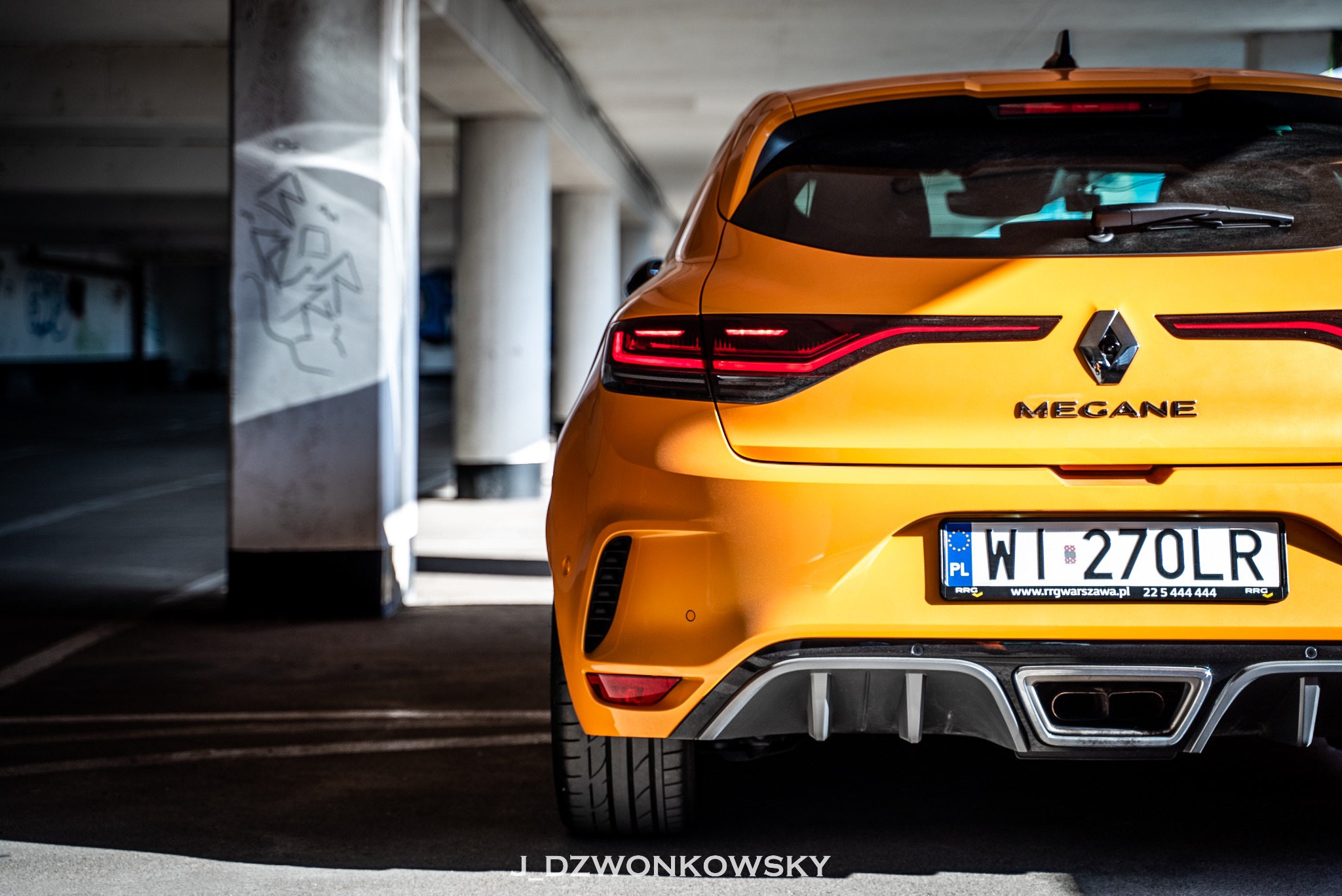 Żółty samochód Renault Megane zaparkowany w garażu podziemnym, widok z tyłu na tablicę rejestracyjną i dyfuzor.
