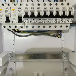 Rozdzielnica elektryczna z zamontowanymi bezpiecznikami różnicowoprądowymi i nadprądowymi marki IDEAL, widoczne przewody elektryczne podłączone do górnej i dolnej listwy.