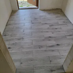 Ułożona podłoga z płytek imitujących drewno w przejściu do ogrodu, widoczne niedokończone obramowanie drzwi.