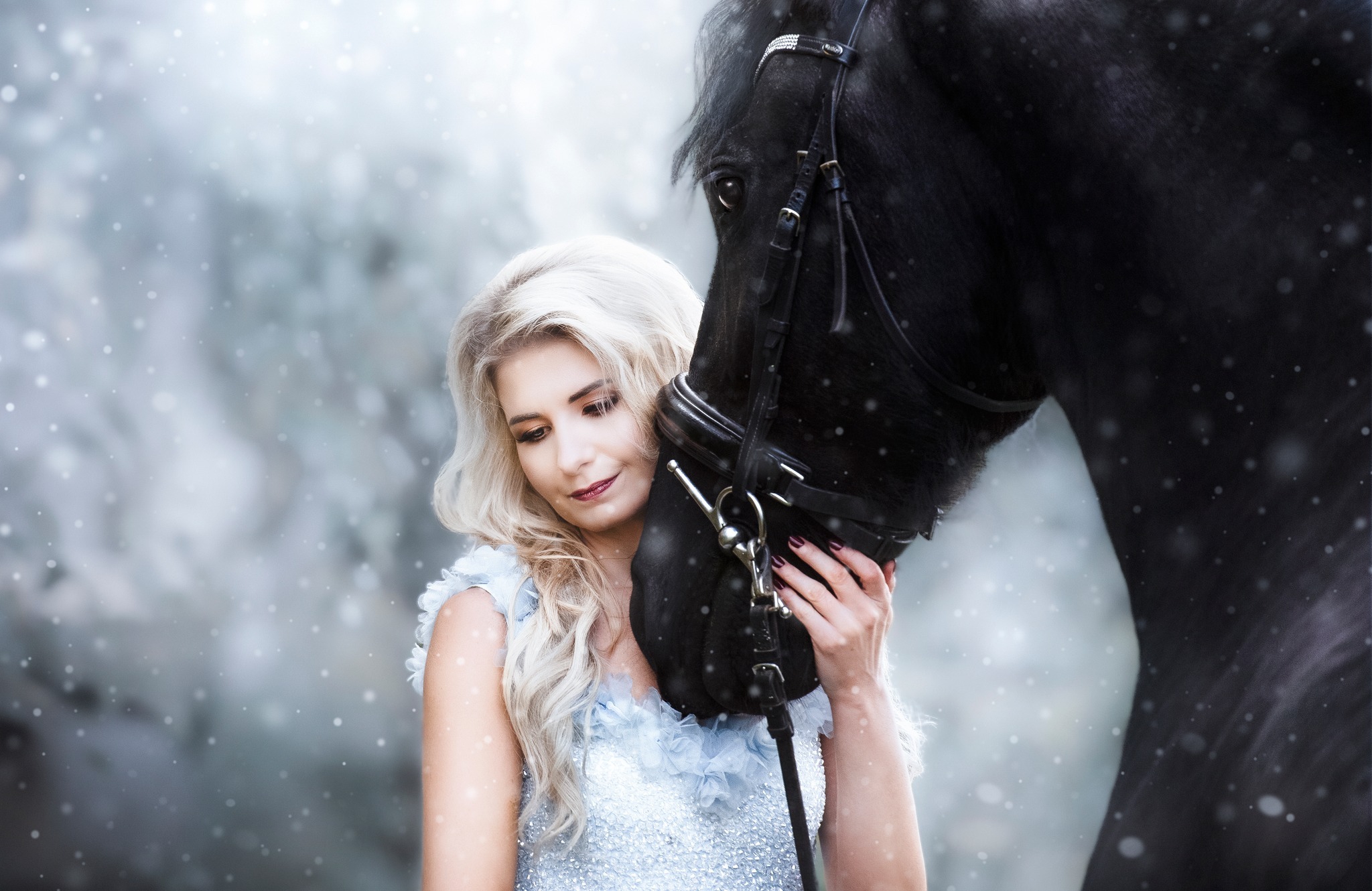 Blondwłosa kobieta w błyszczącej sukni, delikatnie obejmująca czarnego konia na tle zimowego krajobrazu z padającym śniegiem.