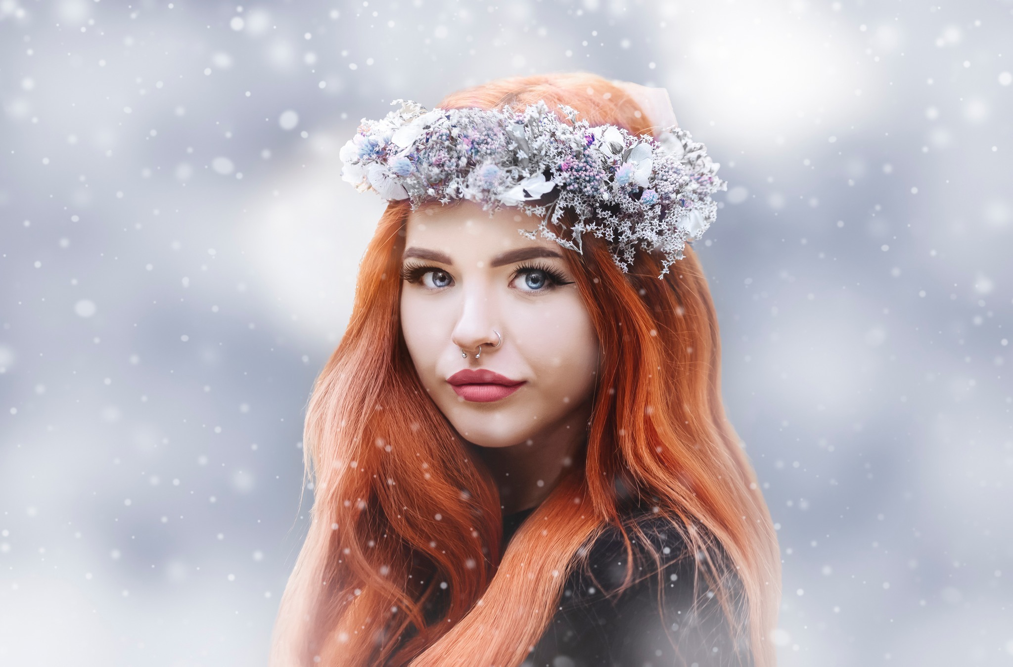 Portret młodej kobiety z rudymi włosami i niebieskimi oczami, noszącej srebrzysty wianek z suszonych kwiatów na głowie, na tle padającego śniegu.