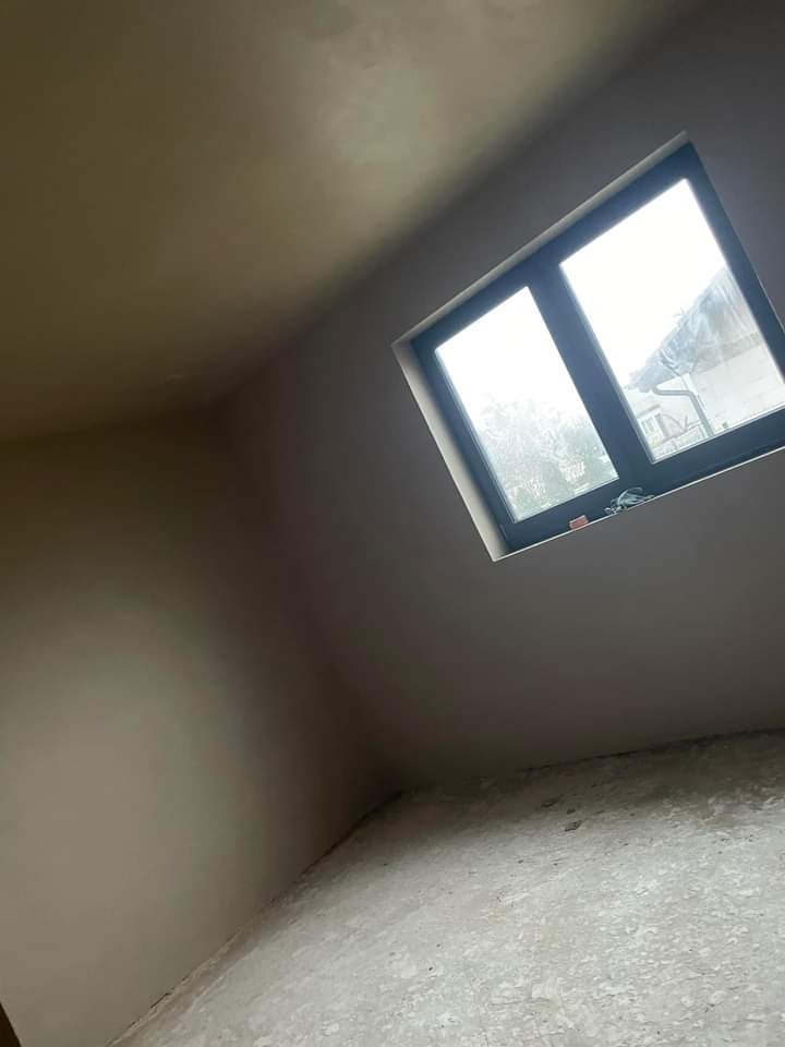 Świeżo otynkowane wnętrze poddasza z małym oknem, widoczne niedoskonałości na podłodze przed sprzątaniem.