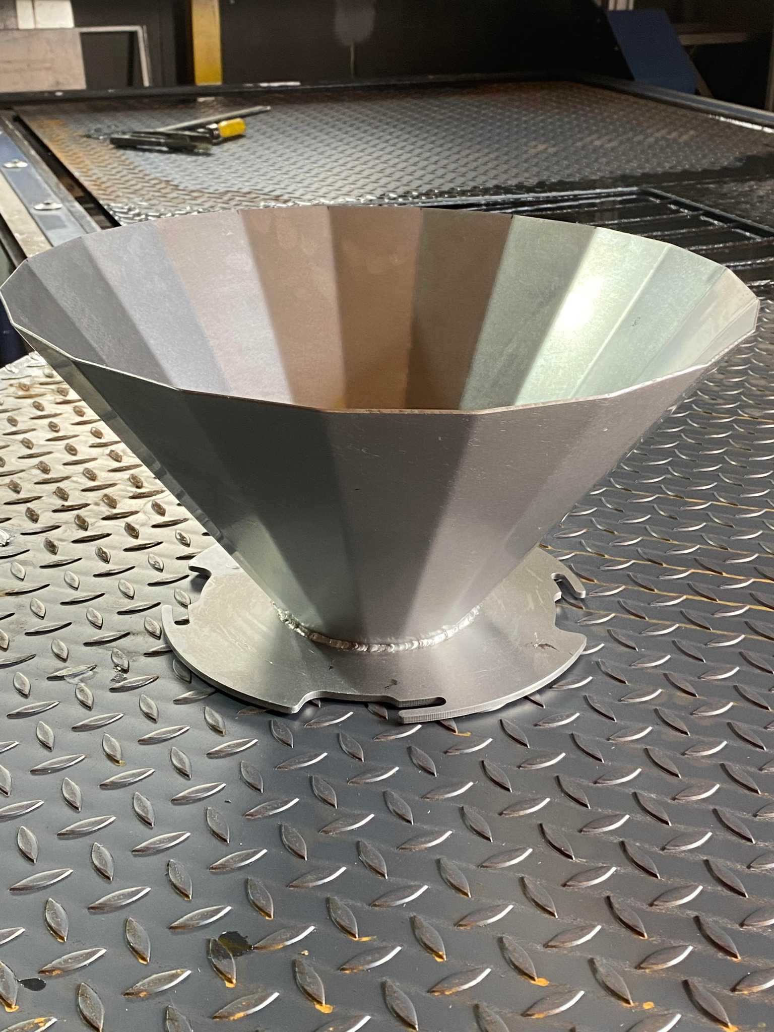 Stożkowy element metalowy z podstawą, wykonany z blachy i spawany, leżący na metalowej powierzchni z fakturą łezki.